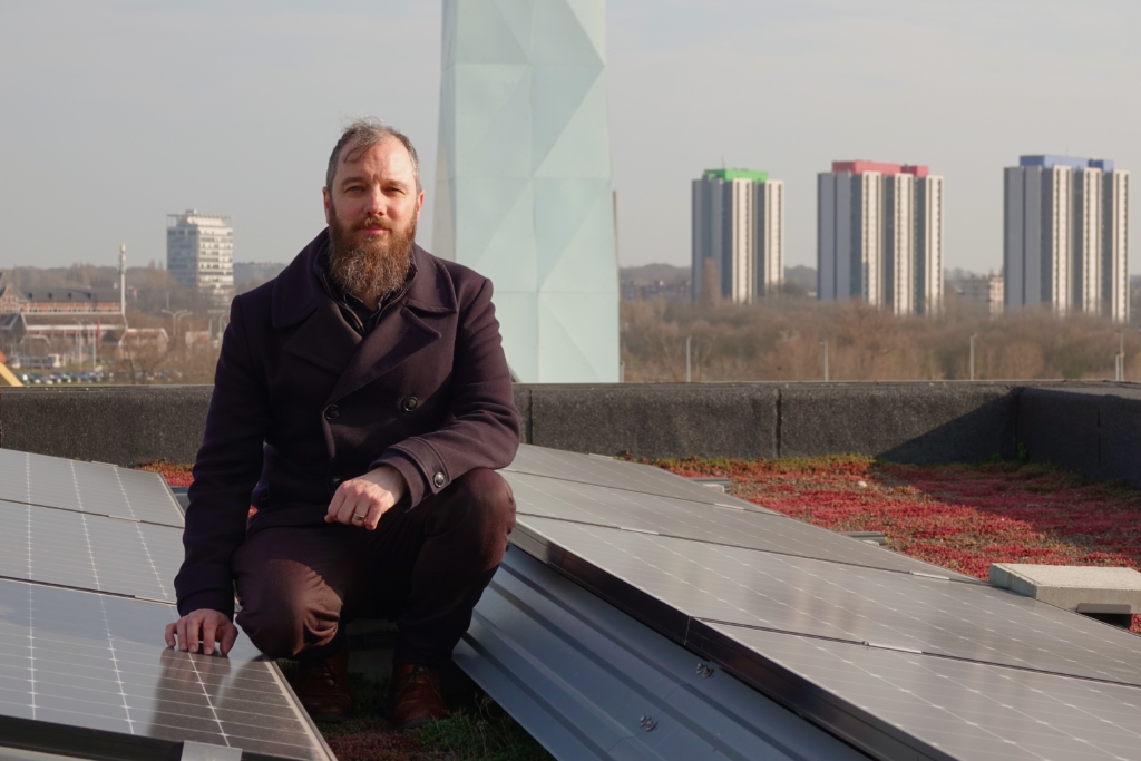 Jan Wouters op het dak van een gebouw op Nieuw Zuid naast zonnepanelen en de verwarmingstoren op de achtergrond