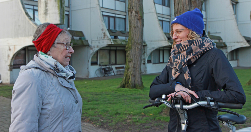 Lynn met de fiets in de Arena wijk. Ze komt een huurder tegen waarmee ze een babbeltje doet.